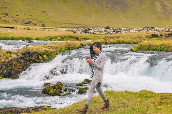 Nainen kävelee vesiputouksen ohi Islannissa. Tyttö turisti rento vaatteet vierailevat islantilainen luonto maisema — kuvapankkivalokuva