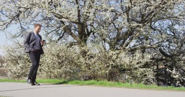 Junger urbaner Geschäftsmann mit Smartphone im Stadtpark unterwegs — Stockvideo