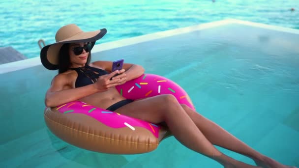 Verão Férias Mulher de biquíni no donut inflável usando telefone na piscina — Vídeo de Stock