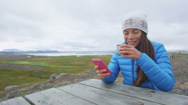 Woman outdoors using smartphone drinking coffee — стоковое видео