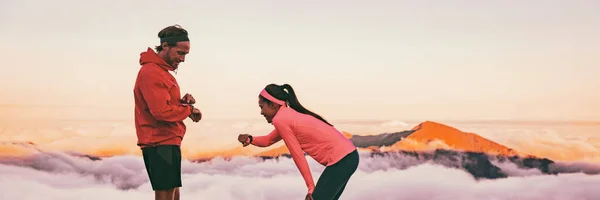 Runners tired breathing after training looking at their wearable tech sports watch checking heart rate health data. Two athletes couple running together in outdoors mountain banner panorama — 图库照片