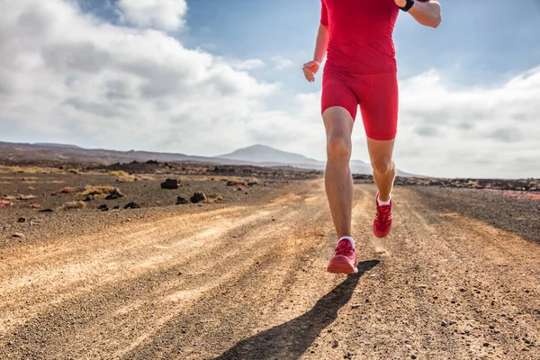 Trail runner athlete man running on dirt mountain path in red compression clothes outfit and running shoes for extreme terrain. — Stock Photo, Image