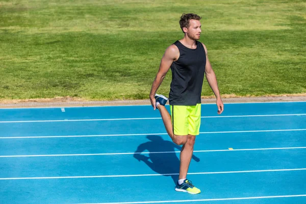 Futó atléta férfi csinál bemelegítő quad izmok csinál láb edzés előtt edzés futópálya a stadionban. Edzés és sport fitness kocogó felkészülés a versenyre. — Stock Fotó
