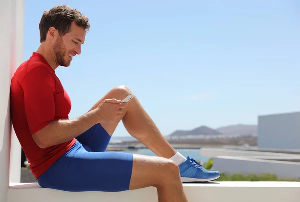 Hombre de deporte de fitness utilizando la aplicación de teléfono móvil después del entrenamiento relajante sentado en el balcón de casa. Tecnología y deportes atleta celebración de teléfono inteligente. Estilo de vida activo y saludable. —  Fotos de Stock