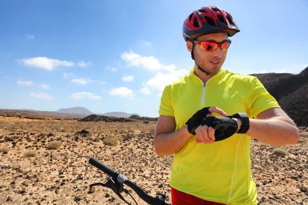 Sport fitness watch mountain biker on mtb bike using smartwatch app for fitness challenge. Young man athlete using his wearable tech biking in mountains nature landscape. — Stock Photo, Image