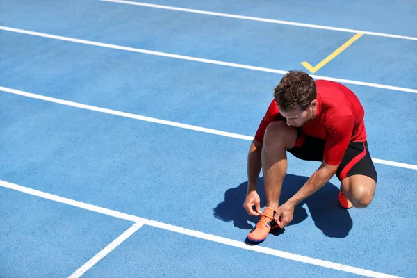 Athlete sprinter getting ready to run tying up shoe laces on stadium running tracks. Man runner preparing for race marathon training outdoors. Fitness and sports. — Stock Photo, Image