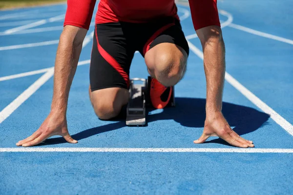 Runner athlete starting running at start of run track on blue running tracks at outdoor athletics and fiel stadium. Sport and fitness man lower body, legs and running shoes going sprinting. — Stock Photo, Image