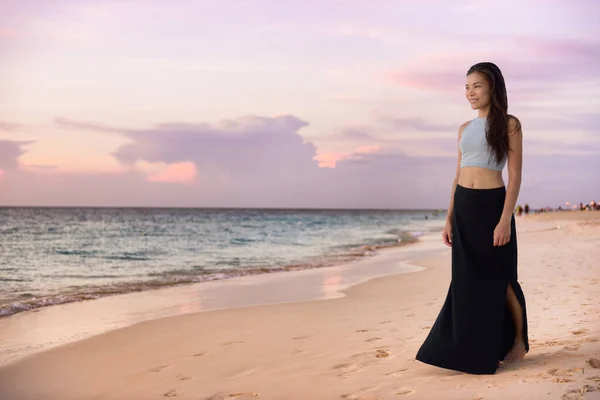 Donna modella asiatica che cammina sulla spiaggia al tramonto rilassandosi durante le vacanze di lusso nei Caraibi indossando abiti maxi gonna di moda per la notte in vacanza estiva. Ragazza cinese godendo vista dell'oceano. — Foto Stock