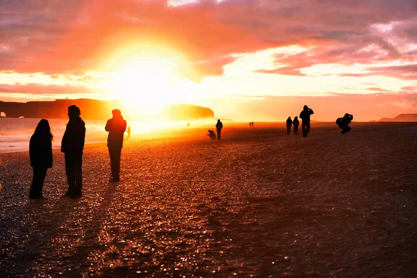 Iceland travel tourists walking on reynisfjara Black Sand Beach. Landscape photography tourists taking pictures, silhouettes of people against sun flare at sunset. — 图库照片