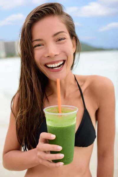 Yeşil smoothie detoks içeceği gülümseyen Asyalı kadın sahilde sebze suyu içiyor. Bikini yüzdükten sonra kahvaltı içeceğiyle mutlu kız portresi. Sağlıklı yaşam tarzı çok ırklı model. — Stok fotoğraf