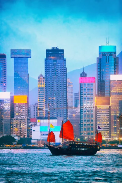 Vista del horizonte de Hong Kong al anochecer del puerto de Victoria desde el lado de Tsim Sha Tsui con letreros de neón iluminados por la noche. Vista nocturna con bote basura en el río en la ciudad asiática, Hong Kong, China. — Foto de Stock
