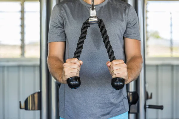 Fitness man exercising triceps muscles in the gym with pull-down ropes fitness equipment machine attachement. Arms strength training at health club. — 스톡 사진