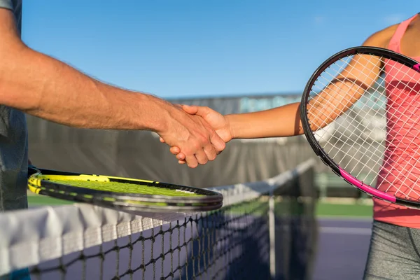 Jugadores de tenis estrechando la mano en la red de la corte al final del juego divertido. Hombre y mujer jugando al tenis recreativo apretón de manos con raquetas de tenis. — Foto de Stock
