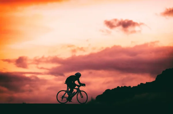 Rennradfahrer, der nachts unterwegs ist. Silhouette eines männlichen Athleten beim Training im Sonnenuntergang — Stockfoto