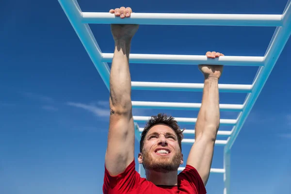Fitness monkey bars man training arms muscles on jungle gym outdoors in summer. Athlete working out gripping climbing on ladder equipment at sport athletics centre