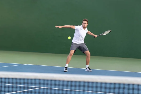 Professional tennis player athlete man focused on hitting ball over net on hard court playing tennis match with someone. Sport game fitness lifestyle person living an active summer lifestyle — 스톡 사진