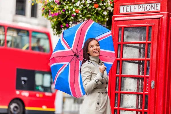 Londýnská turistka s vlajkovým deštníkem, telefonní budkou, červeným velkým autobusem. Evropa cestování destinace Asijská dívka s britskými ikonami, červená telefonní budka, double decker hop na hop z autobusu ve slavném městě — Stock fotografie