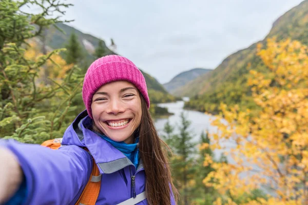 Selfie asian girl hiking in autumn nature mountains. Happy hiker woman taking smartphone picture holding phone at scenic viewpoint in fall mountain landscape outdoors. Forest park travel lifestyle. — Stock Photo, Image