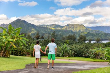 Couple tourists walking on Hawaii vacation. Two young people relaxing in Hanalei Bay resort in Kauai, Hawaii travel beach destination with Kauai mountains in the background clipart
