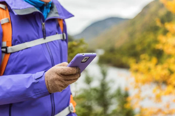 Person hiking in nature using smartphone app with touch screen tech gloves during hike in autumn travel adventure in mountain forest outdoors. Beautiful landscape background. — Stock Photo, Image