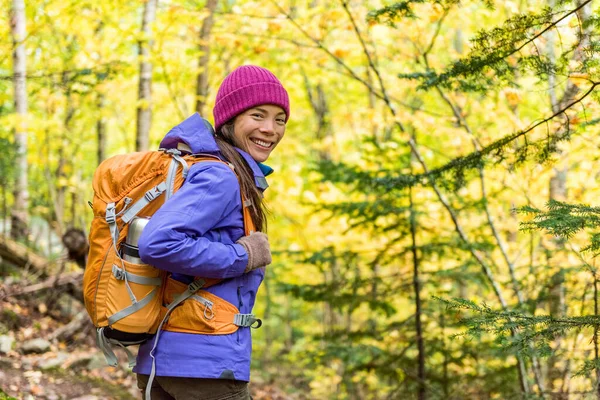 Happy backpacker girl hiking in autumn forest. Young asian hiker woman in outdoor gear for cold weather with backpack looking at camera enjoying walking in nature outdoors in fall season. — Stok fotoğraf