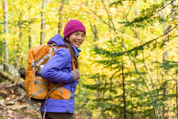 Gelukkige backpacker meisje wandelen in de herfst bos. Jonge Aziatische wandelaar vrouw in outdoor gear voor koud weer met rugzak kijken naar camera genieten wandelen in de natuur buiten in het najaar. — Stockfoto