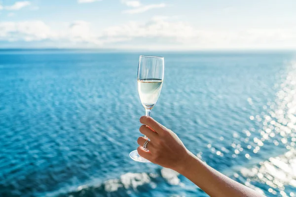 Champagne glass womans hand toasting on ocean background at luxury cruise ship during sunset. Travel vacation for honeymoon, lady holding flute wearing wedding ring. — Stock Photo, Image