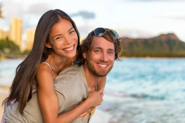 Casal apaixonado nas férias de viagem do Havaí. Mulher asiática feliz piggybacking no homem caucasiano, pessoas multiculturais. Retrato de jovens adultos saudáveis na praia de Waikiki, Honolulu, Havaí — Fotografia de Stock