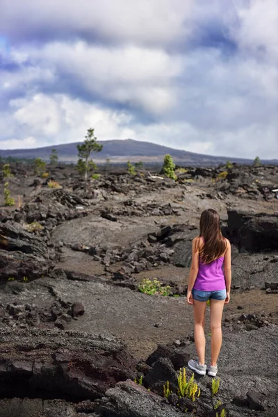 Woman hiking in volcanic rocks on volcano of Big island of Hawaii, USA. Tourist hiker walking on volcanic black rocks during summer traveling holidays — Stock Photo, Image