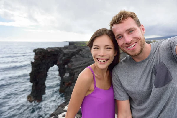 Selfie echtpaar op reis in de natuur Hawaï vakantie. Jongeren die een telefoonfoto maken bij de Holei Sea Arch, toeristische attractie op Big Island in het Volcanoes National Park — Stockfoto