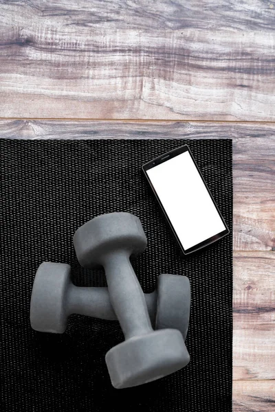 Gym dumbbells on fitness mat showing phone app. Weights on exercise yoga mat and smartphone for health progress tracking mobile app. Phone showing copy on screen for exercising videos online —  Fotos de Stock