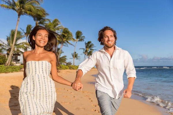 Happy newlyweds couple running on the beach holding hands, honeymoon travel. Asian caucasian multiracial people having fun together — Stok fotoğraf