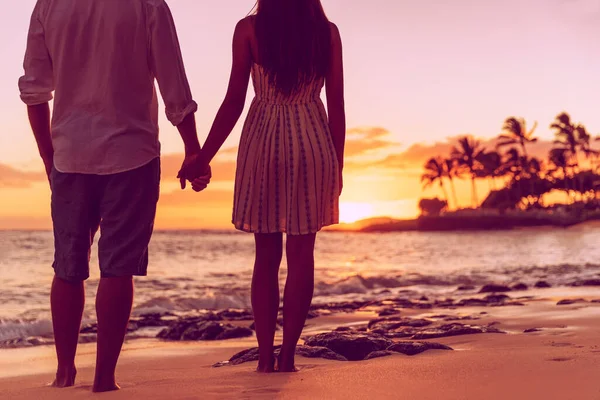Silhouetten von jungen verliebten Paaren, die sich in den Flitterwochen im Sommerurlaub an den Händen halten. Silhouette von Menschen, die gemeinsam den Sonnenuntergang am tropischen Strand beobachten — Stockfoto