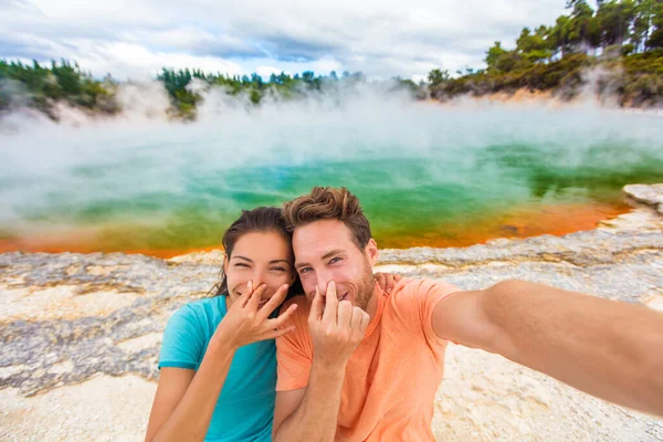 Funny selfie couple tourists at New Zealand pools travel. Young people doing goofy face at smell bad sulfur smell at colorful geothermal hot springs ponds, waiotapu. — Foto de Stock