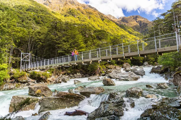 New Zealand hikers tourists crossing river bridge. Couple tramping backpacking woman, man hiking together with backpacks on Routeburn Track trail path. — Stok fotoğraf