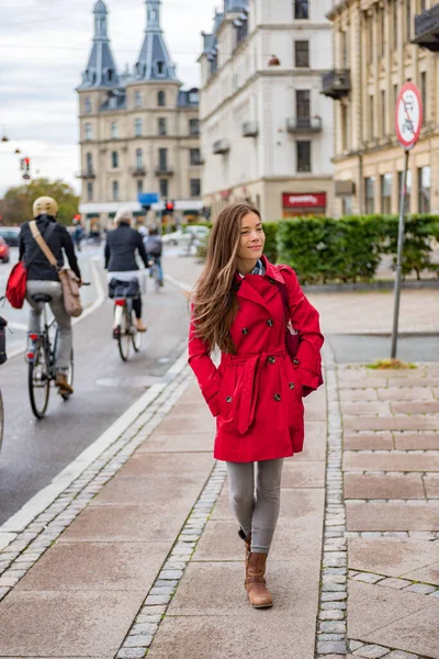 Asian woman walking in red fashion trench coat relaxing outside in Copenhagen city street, Denmark. Europe travel tourism tourist enjoying european lifestyle. — Foto de Stock