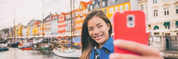Selfie menina turista tirar foto com telefone em Copenhague Nyhavn, famosa atração turística Europa. Mulher asiática no canal de água à beira-mar em Kobenhavn, Dinamarca, Escandinávia. Panorama da bandeira. — Fotografia de Stock