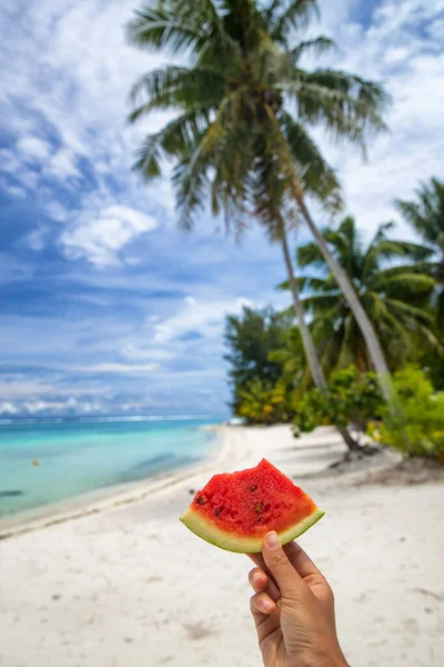 Girl holding bitten watermelong slice on beach background, tropical summer vacation fun. Hand holding fruit snack outside enjoying holidays — Stok fotoğraf