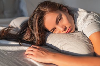 Funny tired lazy asian young woman waking up in bed sleepy morning fatigue with half open eyes cant wake up lying on pillow in bed clipart