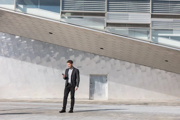 Podnikatel používající mobilní telefon aplikace smskování mimo kancelář v městském moderním městě budovy pozadí. Mladý kavkazský muž držící smartphone pro obchodní práci — Stock fotografie