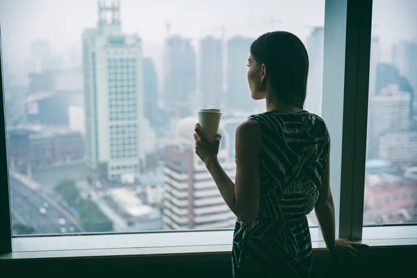 Femme d'affaires buvant du café au travail contemplative regardant par la fenêtre du gratte-ciel de grande hauteur pendant la pause thé du matin. Stress, santé mentale en milieu de travail. Concept d'emploi carrière — Photo