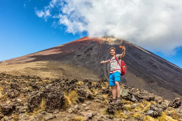 Hiking man on New Zealand Travel taking selfie at Tongariro Alpine Crossing hike trail. Happy hiker tramper phone photo of himself at volcanic mountains background. Summer adventure — Stock Photo, Image