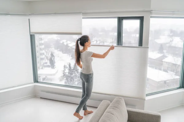 Mujer abriendo cortinas de casa en condominio urbano. Moderno de arriba hacia abajo de abajo hasta la privacidad tonos celulares en la ventana del apartamento manteniendo el calor en invierno con cortina ciega panal. Tonos plisados inalámbricos —  Fotos de Stock