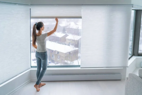 Frau schließt Zelljalousien am Wohnungsfenster und hält Energie und Wärme im Haus mit einem wabenförmigen Jalousievorhang. Akku-Plissee-Farbtöne im modernen Wohnstil. Innenarchitektur — Stockfoto