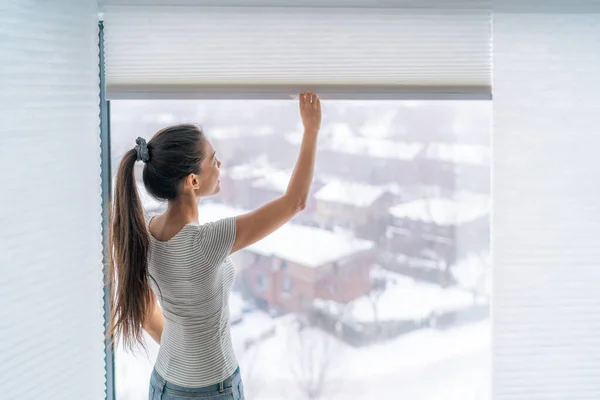 Página de inicio persianas cortinas de ventana mujer apertura sombra ciega durante la mañana de invierno. Chica asiática sosteniendo moderno inalámbrico arriba abajo cortinas de lujo en el interior — Foto de Stock