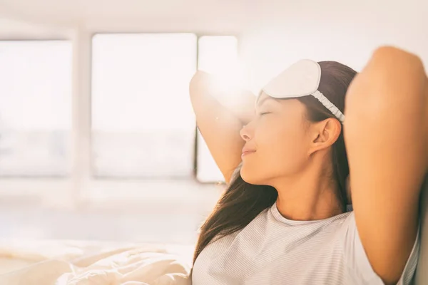 Sova hemma kvinna vakna på morgonen solljus stretching glad efter en god natts sömn känsla utvilad bär ögonmask. Asiatisk flicka säng sova i hotellrum hälsosam livsstil — Stockfoto