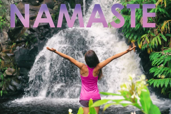Título de NAMASTE escrito como mensaje motivacional por encima de la chica de yoga con los brazos abiertos meditando en la cascada de Hawaii. Bienestar, inspiración mensaje mindfulness — Foto de Stock