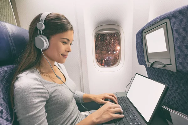 Avión de pasajeros mujer de negocios profesional que trabaja en cabina de avión durante el vuelo con wifi a bordo escribiendo en la tableta de la computadora escuchando música con auriculares. Joven viajero asiático —  Fotos de Stock