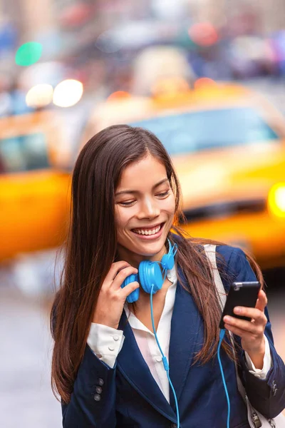 Hoofdtelefoon jonge vrouw lopen in New York stad met behulp van telefoon app luisteren naar podcast of audioboek met oortjes pendelen van het werk. Aziatisch meisje zakenvrouw met behulp van mobiele telefoon — Stockfoto