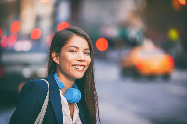 Asiatisk kvinna använder hörlurar gå på NYC New York stadens gatuarbete pendla i eftermiddag skymning. Glad leende multiracial kaukasisk ung flicka urban livsstil — Stockfoto